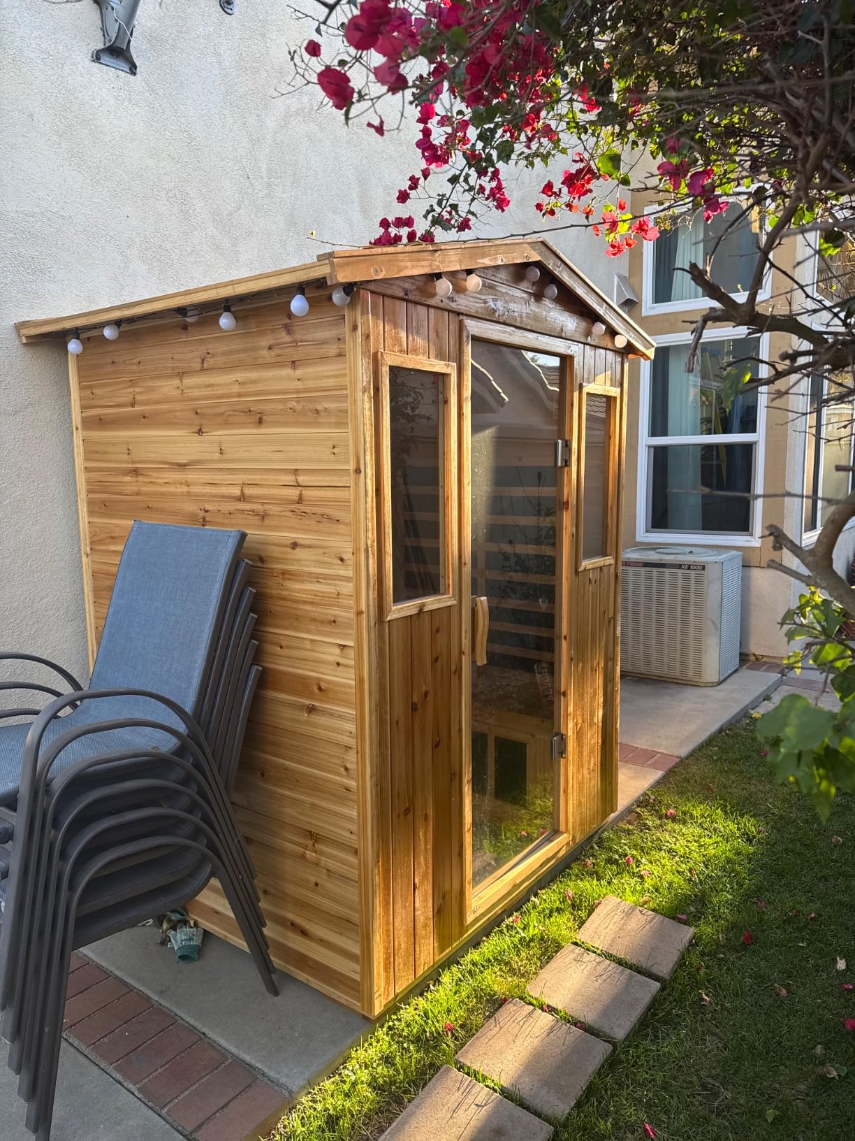Customer’s LTCCDSS outdoor sauna with a peaked roof set up in a side yard next to the house