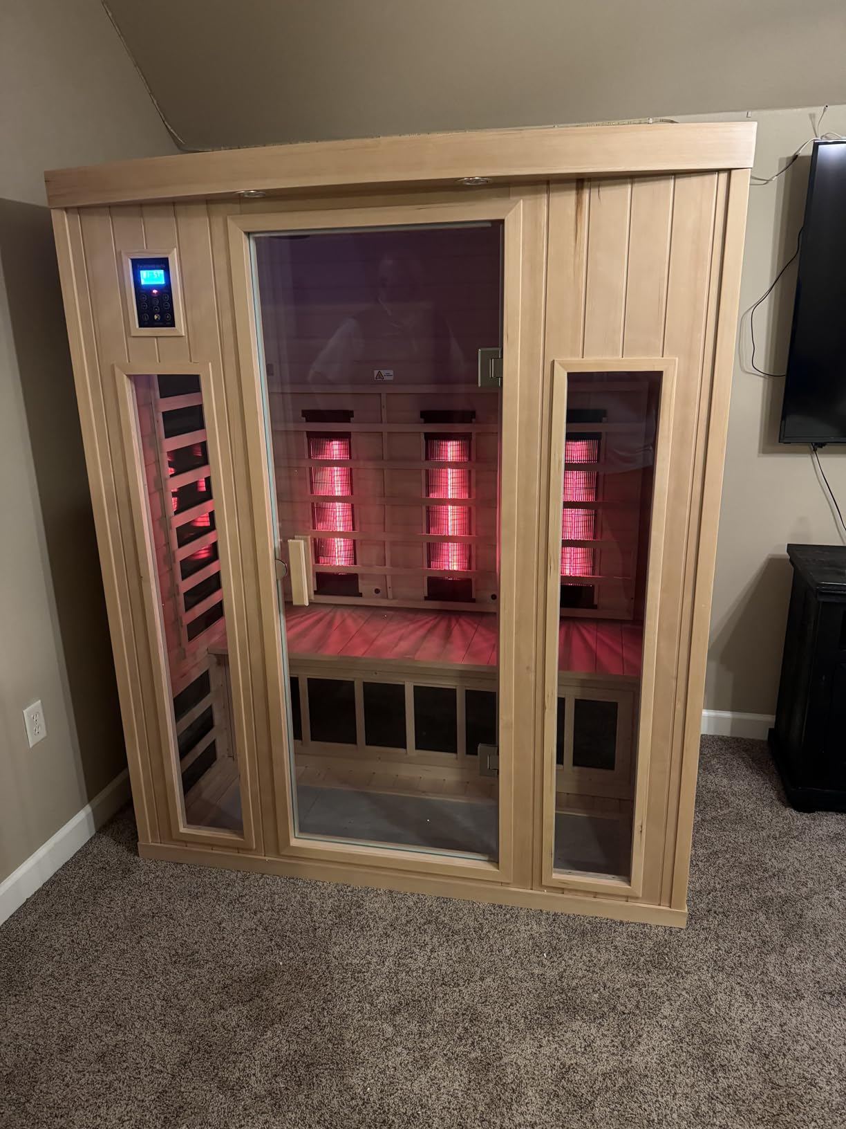 Light wood LTCCDSS infrared sauna with glowing heater panels in a carpeted living room
