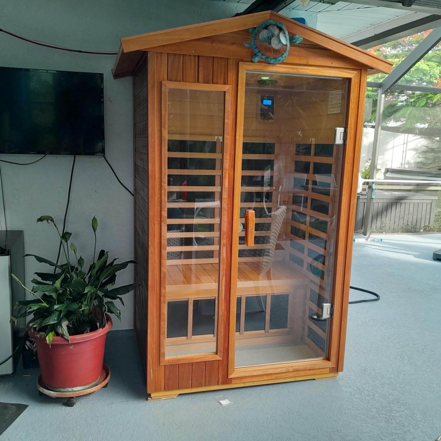 Two-person LTCCDSS sauna with a peaked roof set up indoors beside a potted plant